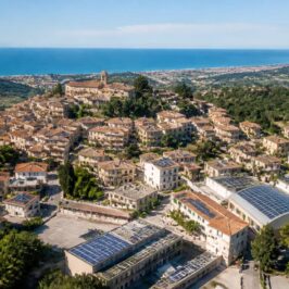 Veduta aerea di un borgo collinare vicino alla costa adriatica con impianti fotovoltaici sui tetti, per un articolo sulle Comunità Energetiche Rinnovabili