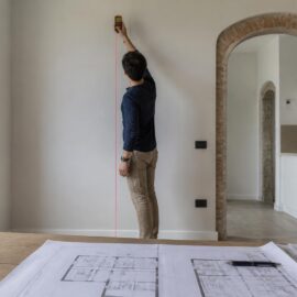 Tecnico che misura l'altezza di una stanza per verificare le tolleranze costruttive rispetto al progetto